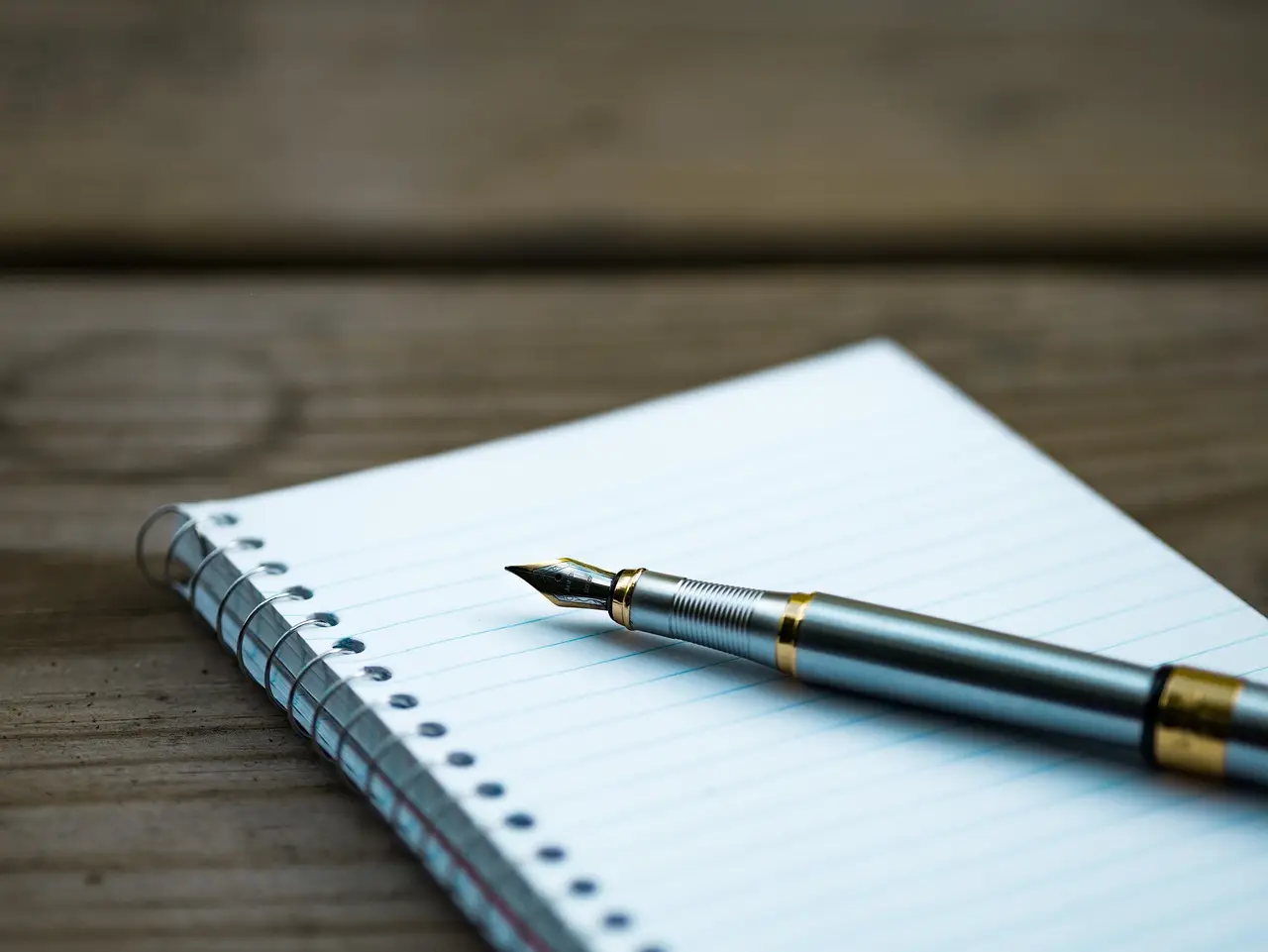 Fountain pen on a lined spiral notebook on a wooden desk