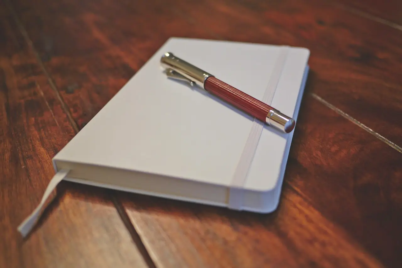 A blank notepad and a plain pen on a plain wooden desk
