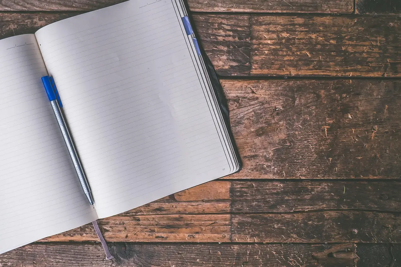 Open lined notebook and a pen on a wooden desk seen from above