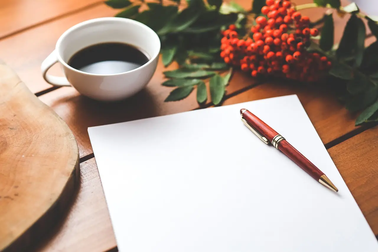 A blank sheet of paper, a red pen, a cup of coffee and red berries on a wooden table